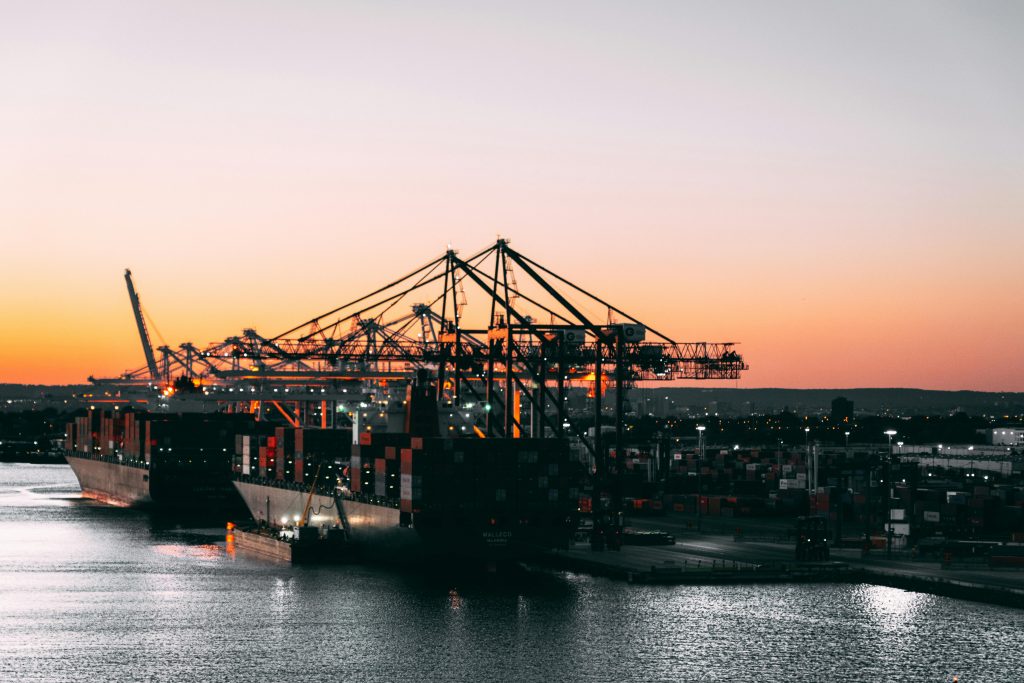 A serene view of cargo ships and cranes at a harbor during sunset, highlighting maritime industry.